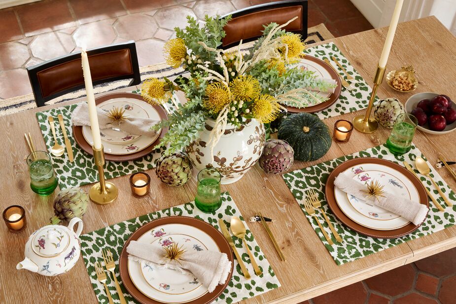 The row of gourds, artichokes, and candles flanking the center arrangement adds a sense of bounty. Shown above: Iconic Leopard Place Mats; Kit Kemp Mythical Creatures Teapot, Dinner Plates, and Salad Plates; Wyatt Chargers; Astrid Napkin Rings; and Oslo Cutlery Sets in Gold. Photo by Matt Albiani.

