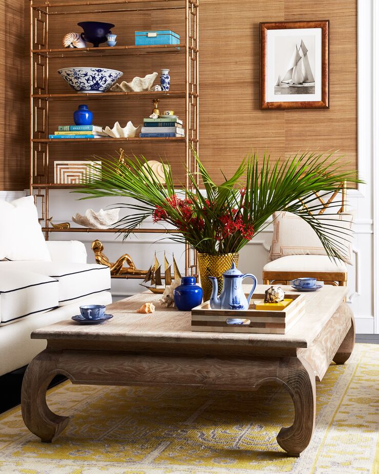 The grass-cloth wallpaper provides a touch of the tropics, while the white panels below the chair rail and the white Kate Sofa keep this room feeling Palm Beach breezy. The étagère and the cocktail table add a dash of chinoiserie, with a layer of glamour courtesy of the golden accents. Find a similar étagère here.
