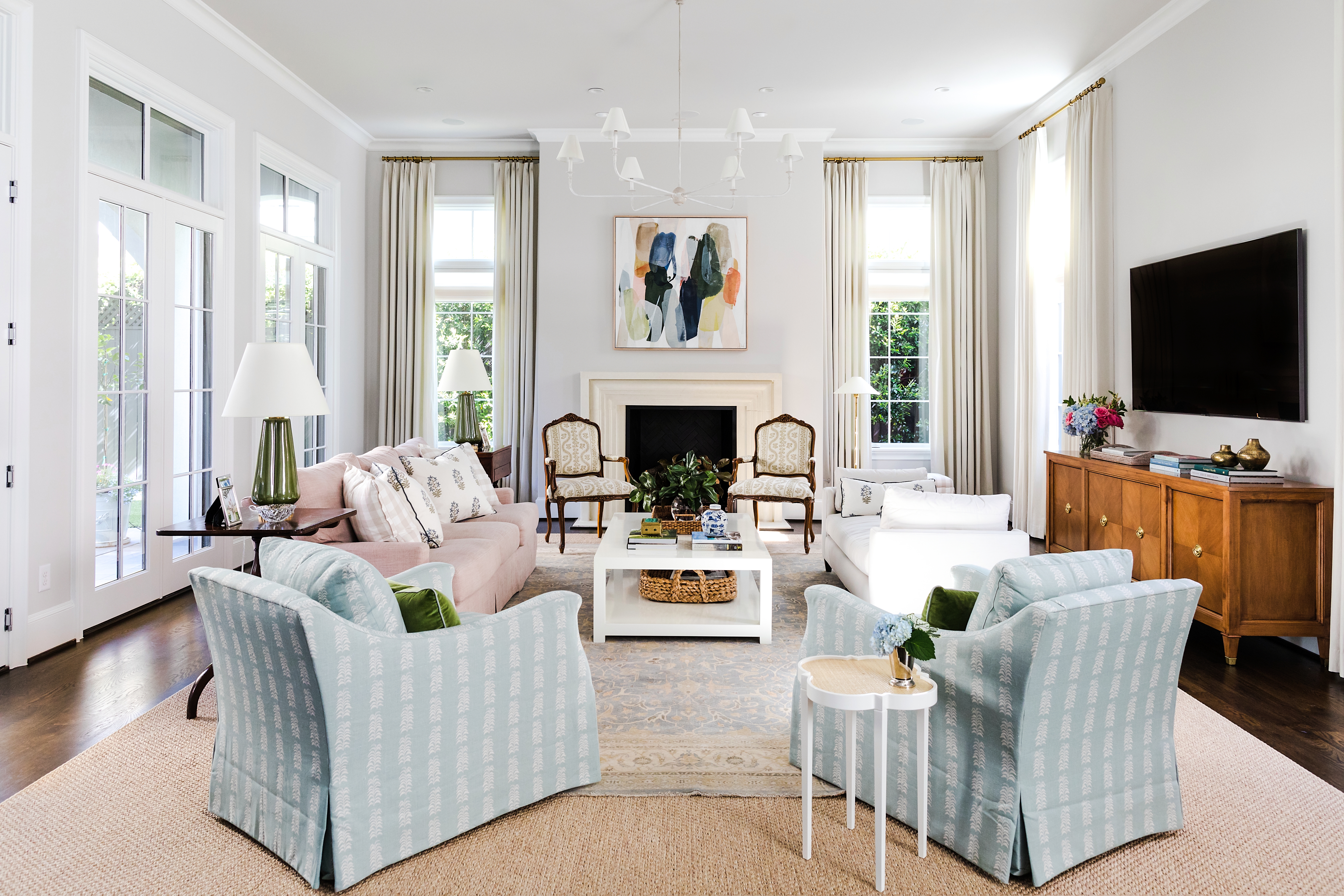 “The palette started with the living room,” Katie says. “The light blue rug that is layered on top of the sisal is theirs that they had sourced on their own, and they loved it. We really loved the idea of contrasting that rug with the sofa. Once the man of the house was on board with a dusty-rose sofa—I never used the word pink!—then all the other colors fell into place.” The table lamps and chandelier are by Visual Comfort.
