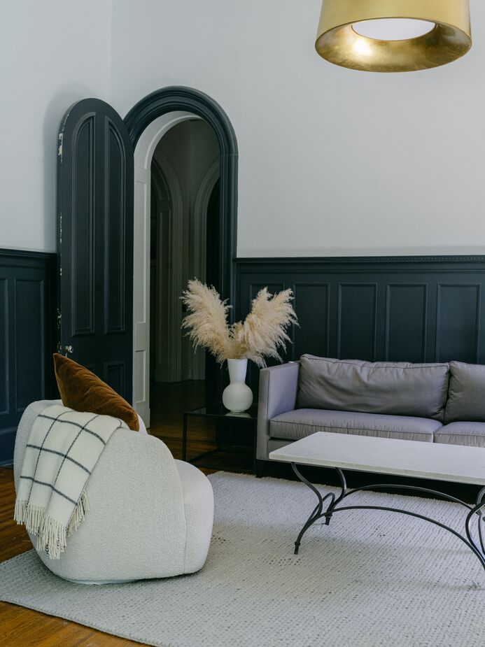 “By toning down the color palette, Ellen and Elliot’s preference for more-modern furnishings makes perfect sense and lends a welcoming and relaxed air to an otherwise intimidating home,” Bethany says. Find a similar lighting fixture here, chair here, and rug here.
