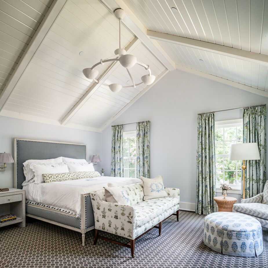 Expanses of pale solids, from the white pitched ceiling to the blue upholstery of the bed, maintain a restful mood amid the patterns of the primary bedroom.
