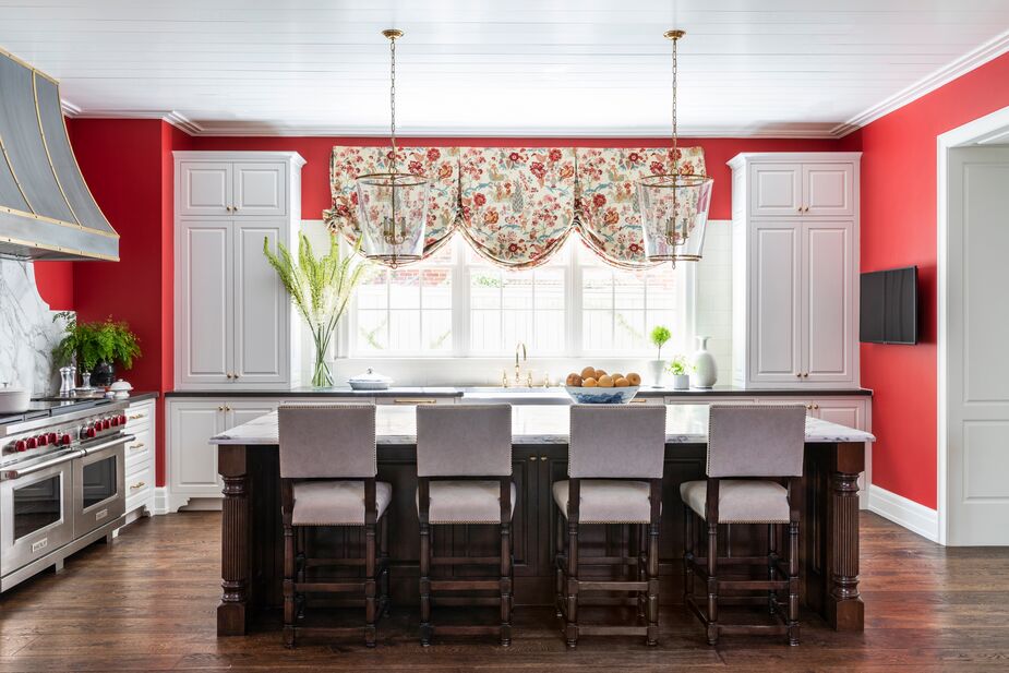 The white cabinetry and the island’s white stone counter balance the kitchen’s red walls and the dark wood of the stool legs and island base. 
