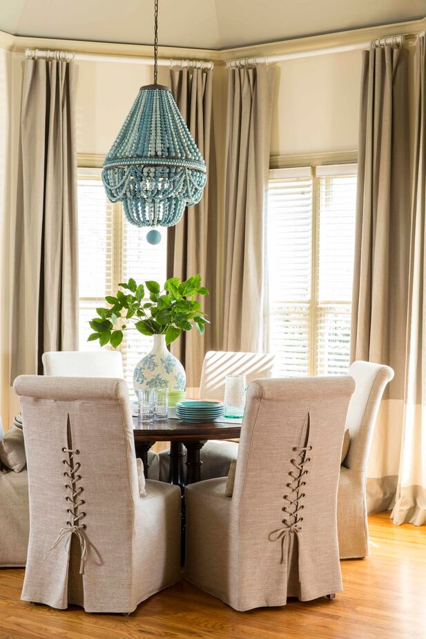 The laced ties bring a bespoke touch to the chair slipcovers, while blue beads add casual chic to the formal shape of the Empire-style chandelier. Find an identical chandelier here. 
