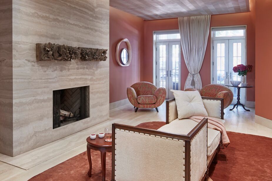 The living room had previously been decorated in neutral tones with a conventional layout. Jennifer warmed it up with pinks and patterns that complement the existing limestone fireplace and blond wood floors. She also introduced more texture via wood veneer in a chevron pattern on the ceiling. 
