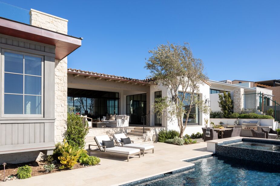 The same limestone tiles used as flooring in the great room surround the infinity pool. The outdoor space includes lounging and dining areas, a kitchen, and a shaded conversation area. 
