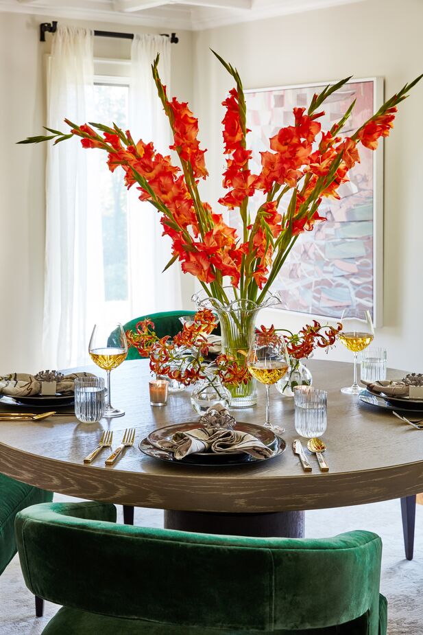 This towering floral arrangement adds drama to the table prior to the meal, but its height would be distracting during it. That’s why it’s surrounded by smaller arrangements that can serve as a centerpiece once the large one is removed before guests sit down. Find the dining chairs here. 
