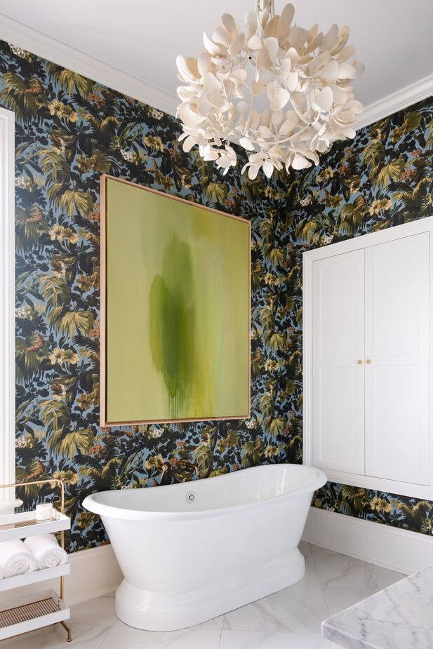 White millwork and a serene green abstract painting temper the vivacious wallpaper, making this bathroom an inviting retreat.
