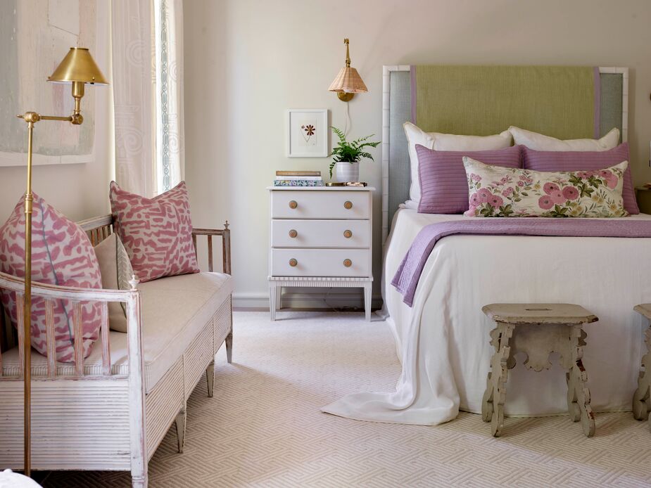 Even an expansive new-build house can have cottage charm. Case in point: this bedroom by Sara Hillery, with its gently distressed bench and stools and soft palette punctuated by orchid and pink accents. Find a similar sconce here and a similar floor lamp here. 
