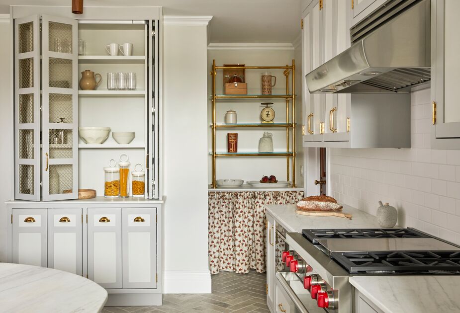 The skirted baker’s rack and the chicken-wire cabinet doors bring a sense of history alongside the kitchen’s throughly modern appliances. 
