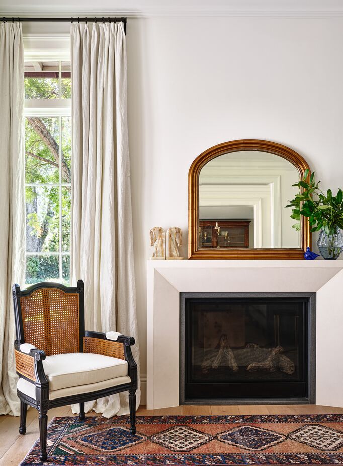 The black finish and elaborate carvings of the Noreen Accent Chair, along with the golden frame of the Mason Mantel Wall Mirror, bring Old World majesty to this room’s neutral palette. The Toikka Bluebird and the dark blue of the vintage floor runner reference coastal beauty. Photo by Read McKendree.
