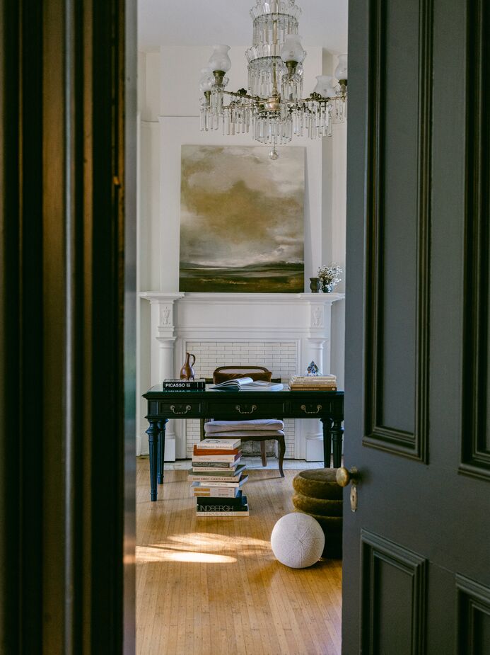 Another of the home’s sitting rooms includes a contemporary white sofa and bucket chairs in addition to the neoclassic black desk and the showstopping crystal chandelier. Find a similar ball pillow here.
 
