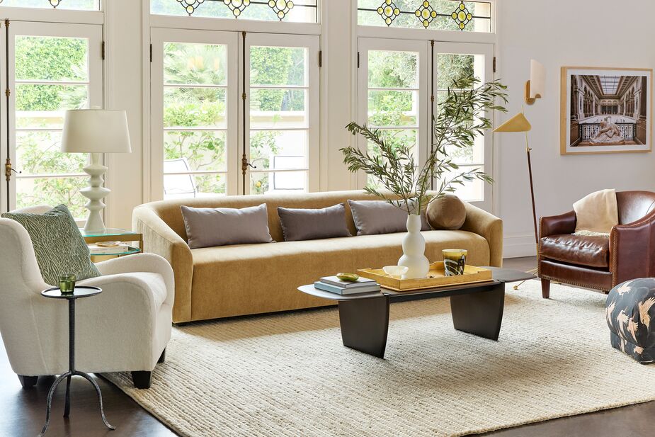 A gold-accented neutral palette and curves galore define this living room. Shown above: the Zola Curved Wingback Chair in Cream Sherpa, the Carver Performance Velvet Sofa in Camel, the Mahogany PI Coffee Table, the Moresby Floor Lamp in Antiqued Brass, and the Ponderosa Rug in Birch.
