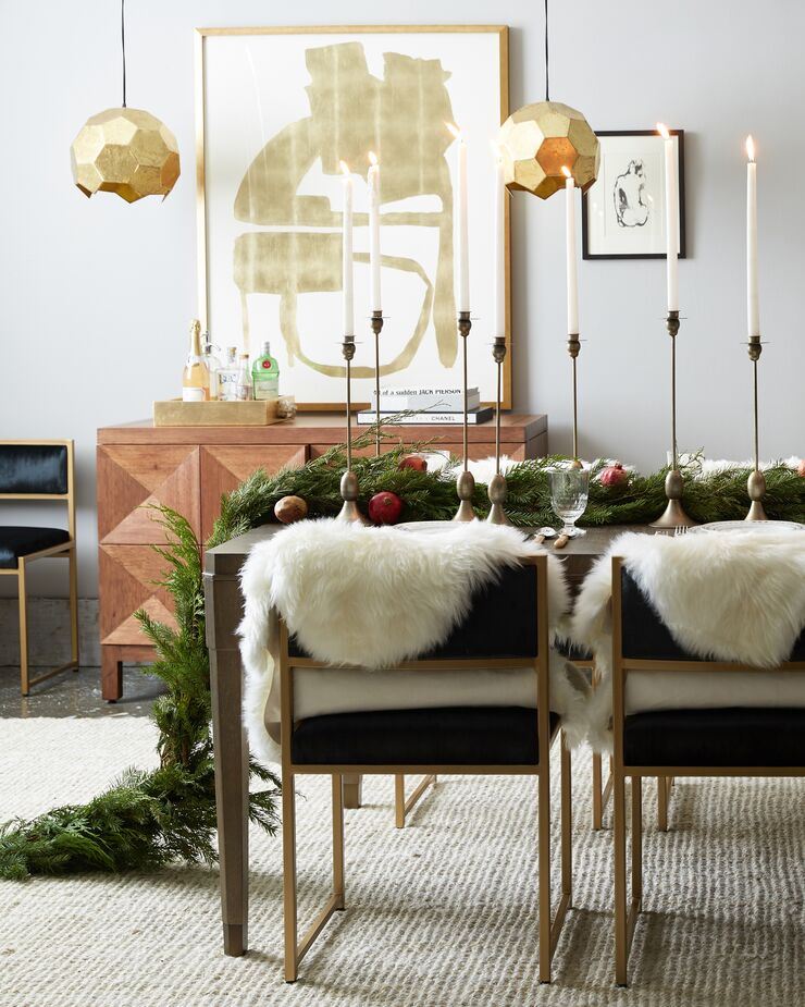 A lush garland that drapes onto the floor makes an especially dramatic table runner. Draping small sheepskins (these are faux) over the backs of chairs adds cozy comfort. Find the golden abstract artwork here.
