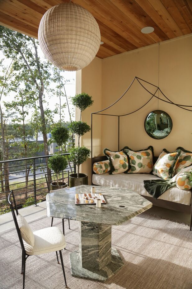 “For my terrace-level covered porch space, I wanted the space to be an invitation to unplug and unwind and to feel like a mini trip to the Mediterranean,” says designer Beth Kooby. The oranges on the pillow fabric and the topiaries play into the theme. “An indoor/outdoor rug softens the floor,” she adds. Find a similar rug here.
