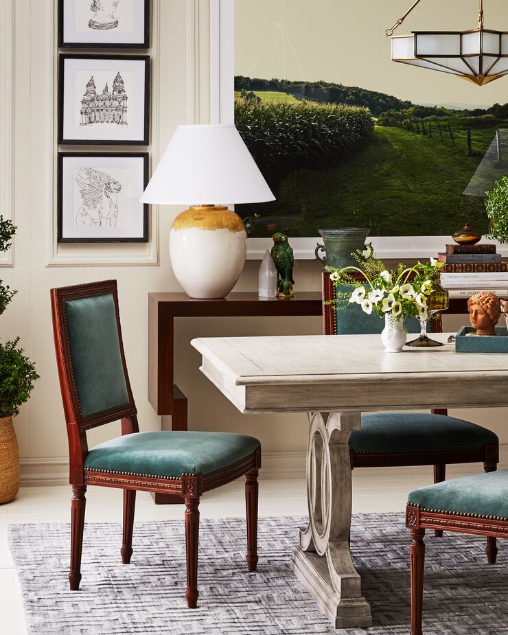 The Exeter Side Chairs (shown here in Jade Velvet) are an update on a classic Louis-style chair. They’re embellished enough to hold their own among the dining table’s ornate base and the gold-trimmed lighting—and they’re also streamlined enough to complement the contemporary large-scale photograph (Cornfield by Christine Flynn) and the smaller whimsical prints by Vikki Chu. 
