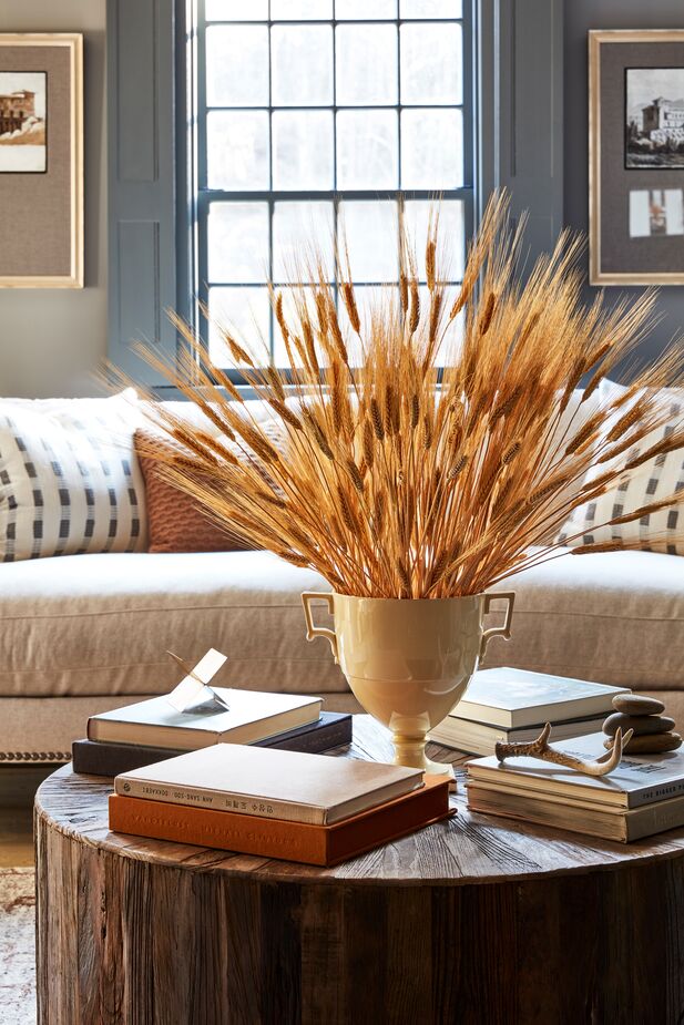 Bundles of wheat displayed in a golden urn gracefully signal autumn’s arrival. Find a similar coffee table here; find the gray-and-white pillows here. Photo by Frank Frances.
