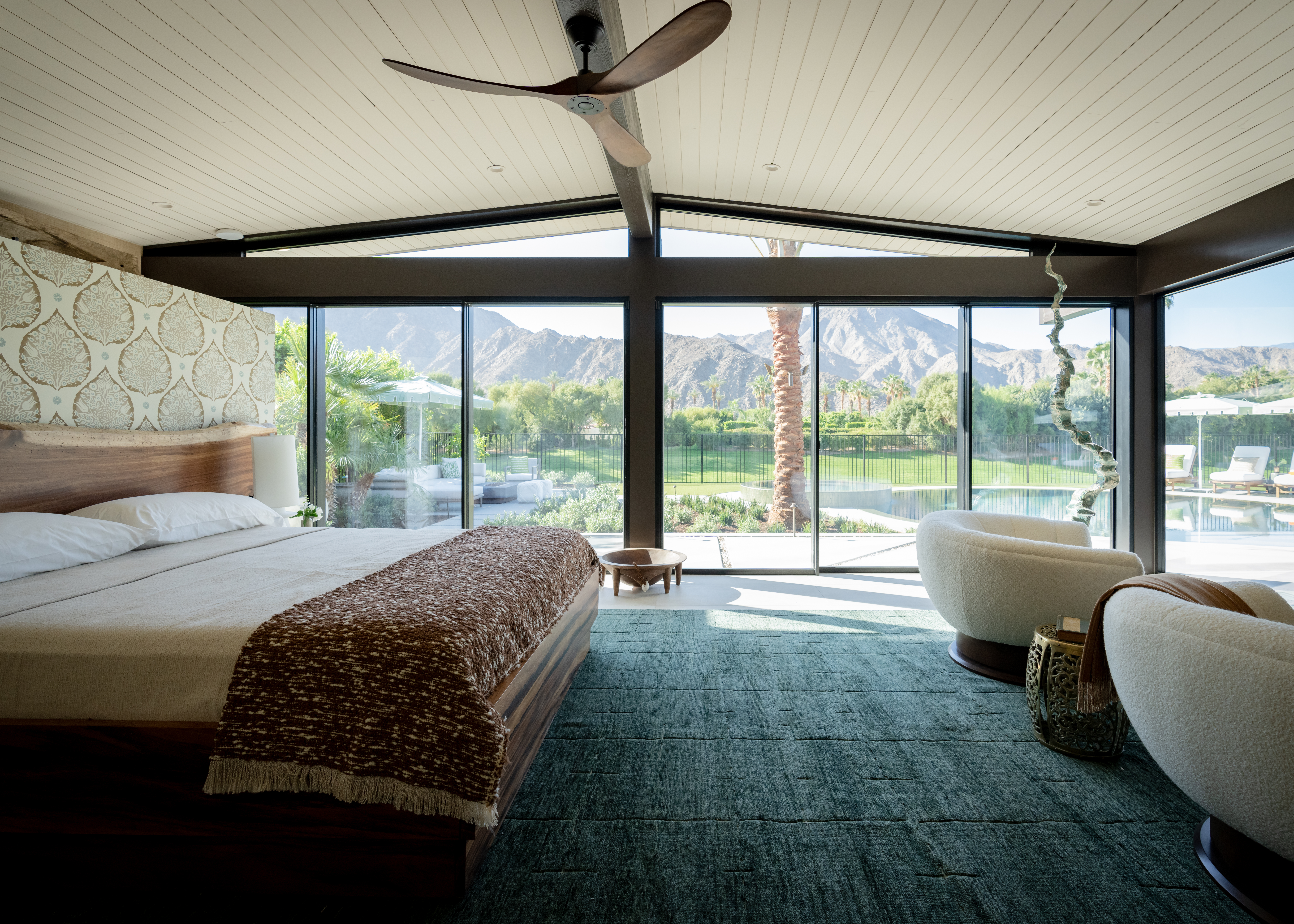 With a view like this, a room doesn’t need much adornment. Chris Barrett of Chris Barrett Design kept things low-key but luxe: a custom bed made of lavishly grained wood with a live-edge headboard, plush swivel chairs (find similar here), a totem-inspired sculpture by Herb Alpert (yes, he’s an artist as well as a musician). Atop the wall with the palm-print paper is a 16-foot Hawaiian canoe from the homeowner’s collection. Find an identical ceiling fan here. 
 

