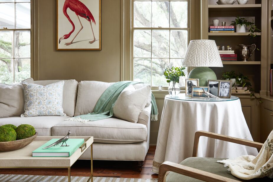 Softer greens, including the Herringbone Throw in Agave, the Dried Moss Balls on the cocktail table, and the table lamp, keep the Brooke Three-Seat Sofa in Flax and the white skirted table from feeling lost amid the taupe-green walls. Find the Audubon print here. Photo by Frank Frances.
