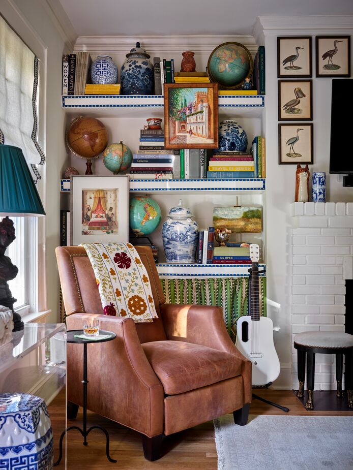 Lathem added the fireplace and the flanking built-in bookcases to the living room during a partial renovation of the 1940s home. This wall is opposite the one shown at top, where artwork is layered over a wallpaper mural. Find the garden stools here. 
