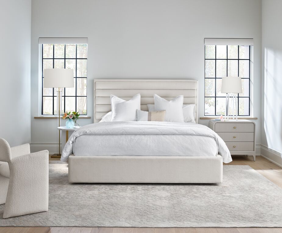 This bedroom all but exemplifies tranquility. Not only does the reeded headboard of the Tranquility Upholstered Bed add glamour, but it also serves as a pampering backrest. The White Carrara Side Table serves as a nightstand on the left; the Elevation Three-Drawer Nightstand is on the right. With its sheepskin-like upholstery, the Morel Armchair adds to the serenity.
