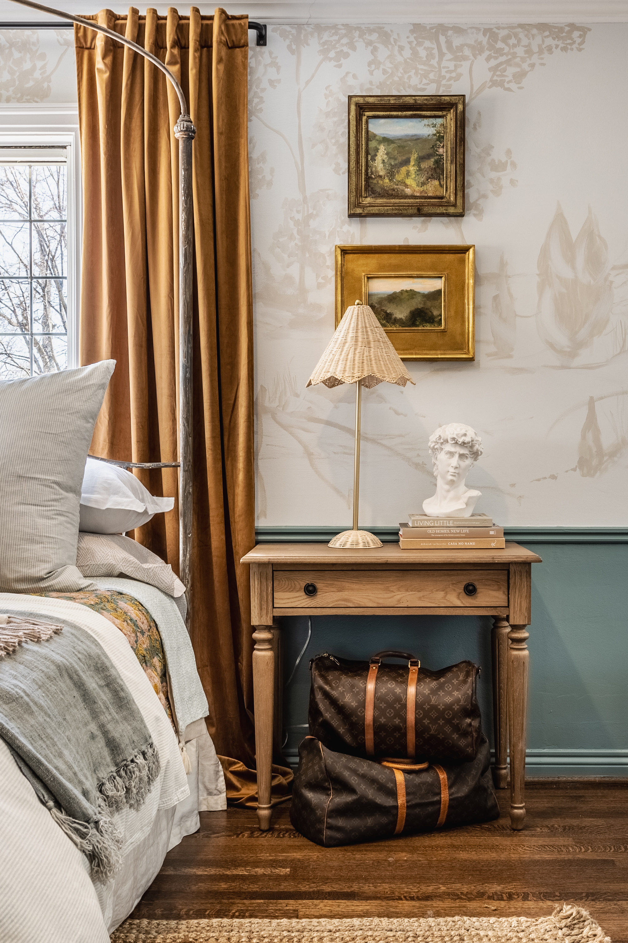 When designing the primary bedroom, MJ Coyle of Michael Jeffrey Design and Blake W. Richardson of BWR LLC clearly envisioned someone who appreciates whimsy almost as much as Old World elegance. How else to explain the rattan parasol lamp perched atop a nightstand with classic turned legs and below two traditional landscapes in lavish golden frames? At the same time, the natural-fiber rug (find a similar one here) provides a contrast to the sumptuous drapes puddling in grand-manor fashion.
