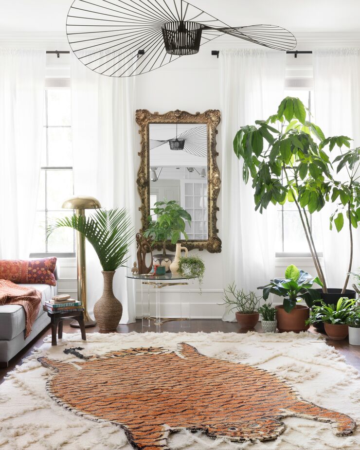 A highly stylized faux tiger-skin rug leans into the “jungle” aspect of urban jungle style. Below that rug is a larger artisanal rug reminiscent of a Moroccan wedding blanket.
