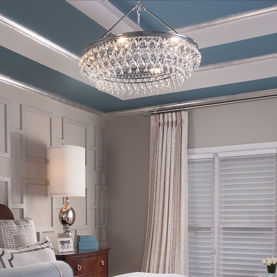 The chrome finish of the Calypso 6-Light Chandelier, along with the silvery nightstand lamp, ceiling molding, and curtain rod, gives this bedroom a contemporary glamour.
