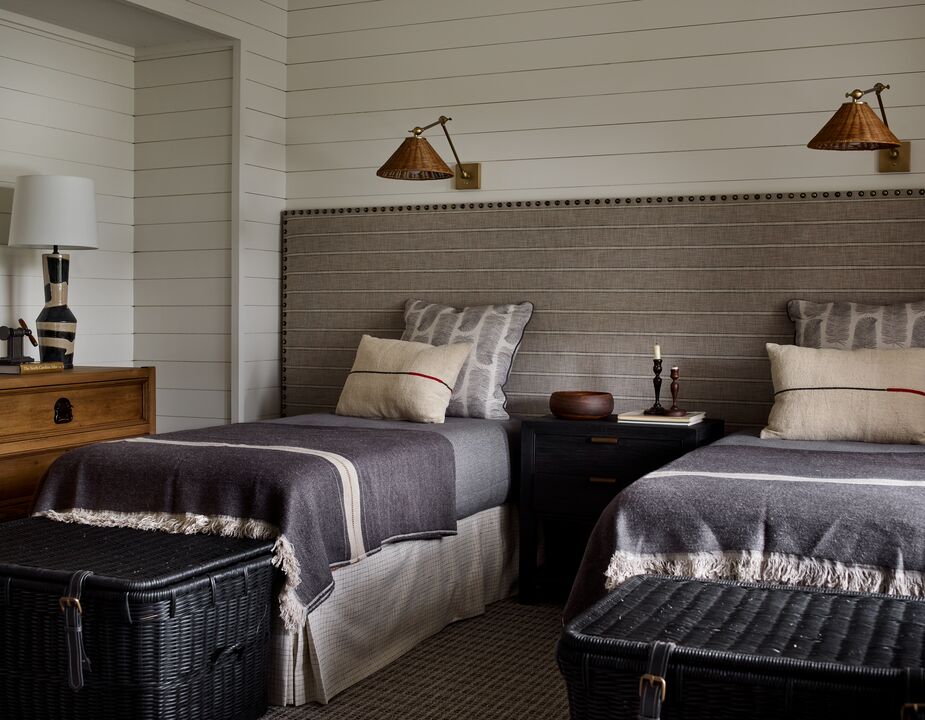 Melanie Millner of the Design Atelier used a large upholstered panel in lieu of headboards in this guest room, adding to a calm cohesiveness. The large wicker basket at the foot of each bed offers easy storage and contributes to the laid-back lodge vibe. See more of this Georgia lake house here. Photo by Emily Jenkins Followill.
