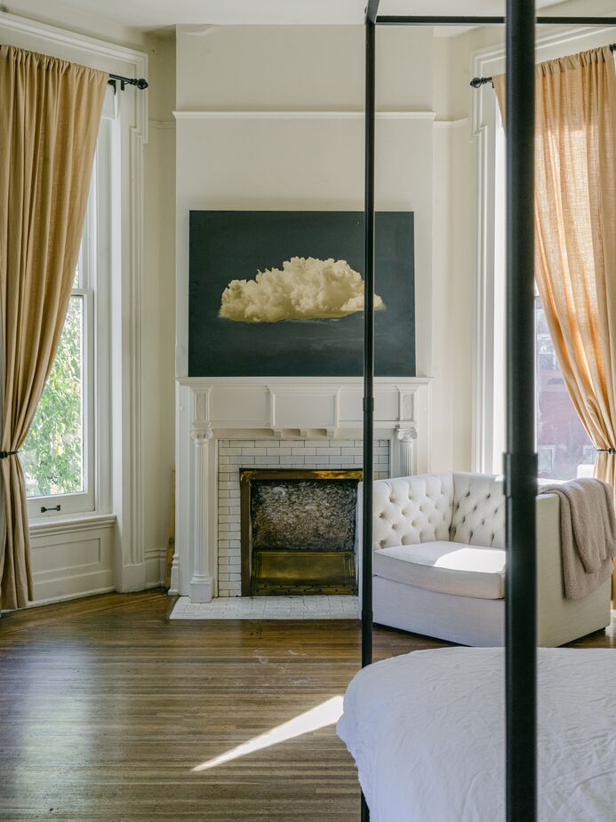 The painting of a cloud atop the mantel captures the dreamy vibe of the white and cream bedroom, one of five bedrooms in the home.
