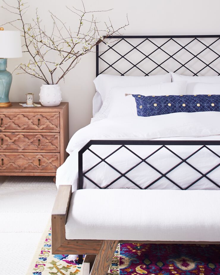 The crisscross pattern of this iron bed’s headboard and footboard adds the “new” to “farmhouse style.” Ditto the colorful rug. Find the bench here.
