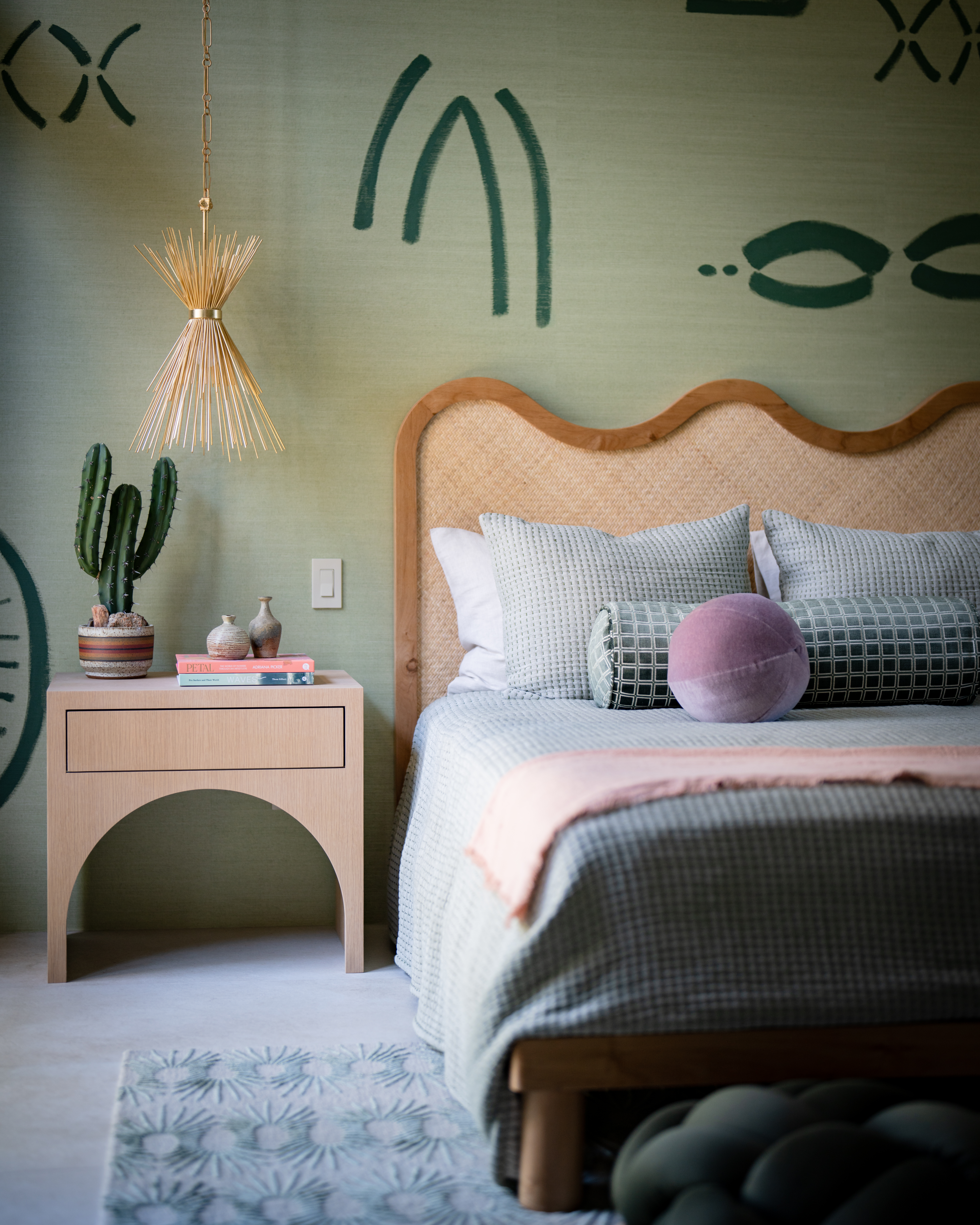 Island Feast, seen in the dining room, inspired the hand-painted grass-cloth mural in this bedroom by Jen Samson of Jen Samson Design. The arch of the nightstand echoes the undulating headboard—and the shape of the ball pillow. 
