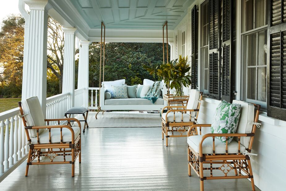 Accessories that would look equally at home indoors, such as an occasional table and a vase, help create a porch that says “Sit and stay awhile.” Comfortable seating, of course, is also key. Find the ottoman here and a similar porch swing here. Photo by Frank Frances.
