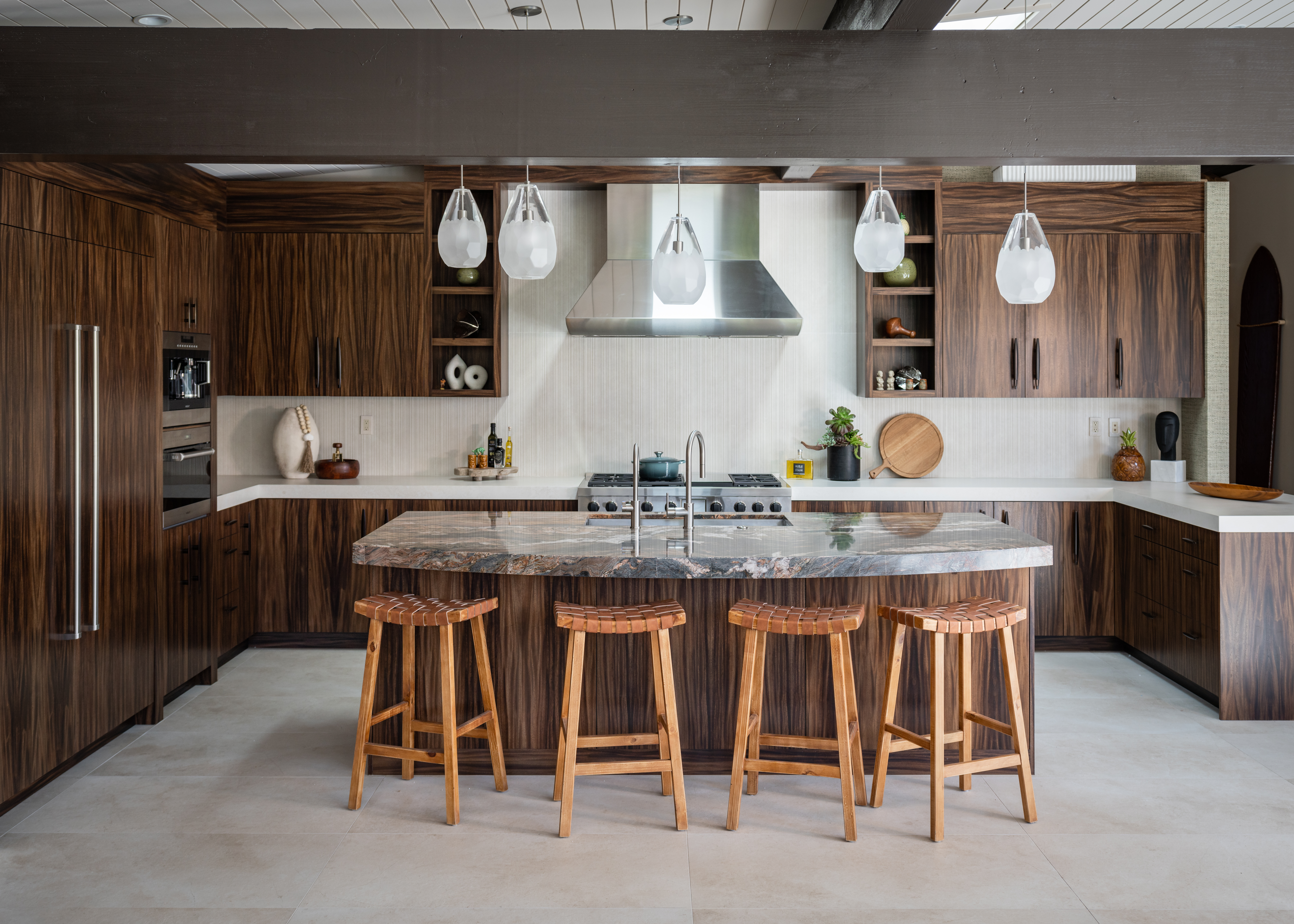 In the kitchen, Donna Johnson of Luxury Designer replaced the vibrant color of the dining and family rooms with richly figured wood cabinets and a stone island counter. Backless stools give the cook an unimpeded view into the other rooms, while staggering the heights of the pendants adds a dash of unpredictability.  
